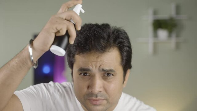 Young handsome man applying spray to hair by looking at camera - concpet of using hair freshener or treatment to protect hair fall.
