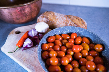 Tomatoes in a pan with bread, chili and onion on a board