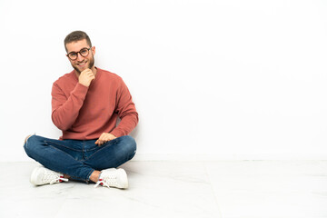 Young handsome man sitting on the floor with glasses and smiling