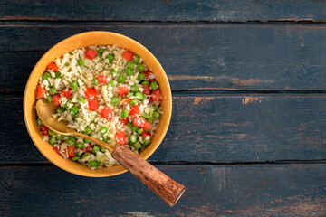 Bowl of cauliflower has tomato and bean on blue wood table.