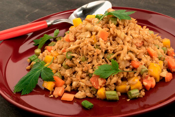 Cauliflower fried rice has vegetable in red dish on wood table.