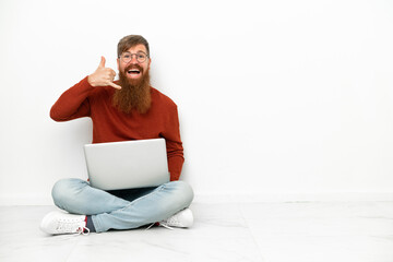 Young reddish caucasian man with laptop isolated on white background making phone gesture. Call me back sign