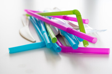 Plates, straws, knives, forks, glasses, disposable plastic objects, photographed closely. Plastic recycling and sales ban.