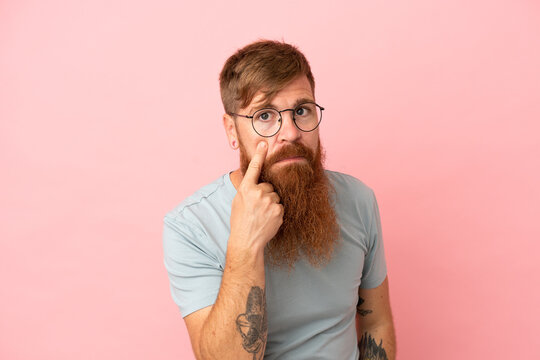 Young reddish caucasian man isolated on pink background showing something