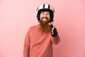 Young reddish caucasian man with a motorcycle helmet isolated on pink background shaking hands for closing a good deal