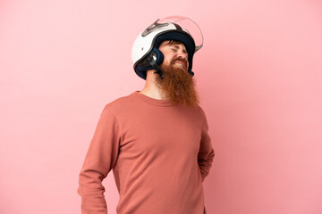 Young reddish caucasian man with a motorcycle helmet isolated on pink background suffering from backache for having made an effort