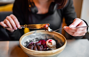 Young woman hand eating chocolate fondant dessert using knife and fork fom bowl