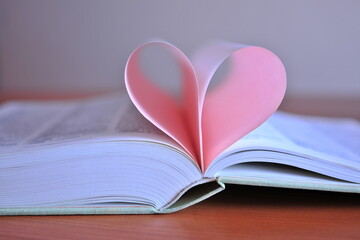 An unfolded book on a table with a pink heart. Blurred background. Copy space.