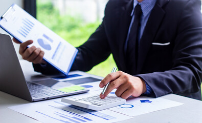 Male finance worker calculates last quarter's earnings figures and points to documents to present, business man checks company income and finance documents, modern business man concept.