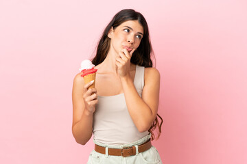 Young caucasian woman with a cornet ice cream isolated on pink background having doubts