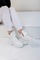 Beautiful female legs in white trousers, white leather sneakers. New collection of women's casual shoes
