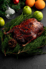 roast duck served on a plate with green branches and decorated with pine cones. Dish on dark christmas background
