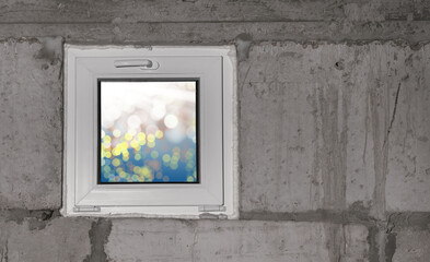 A small plastic window in the dark basement of the house