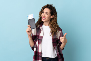 Young caucasian woman isolated on blue background in vacation holding a passport and plane with thumb up