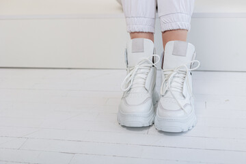 Beautiful female legs in white trousers, white leather sneakers. New collection of women's casual shoes