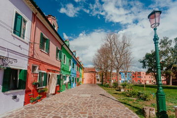 Cozy street with park near colorful private houses of Burano island on sunny day. Venice.