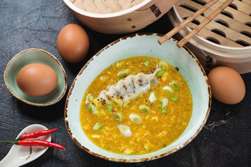 Green bowl with chinese egg-drop soup and steamed dumpling, elevated view on a dark-brown stone background, horizontal shot