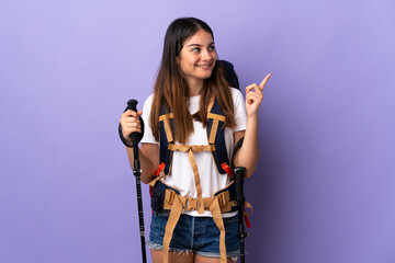 Young woman with backpack and trekking poles isolated on purple background pointing up a great idea