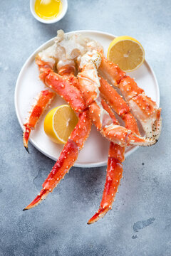 Boiled crab claws served with lemon and butter on a white plate, vertical shot on a light-blue stone background