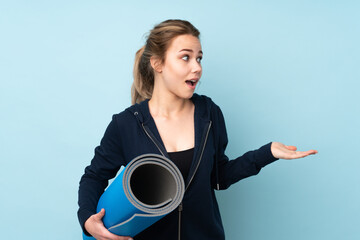 Teenager Russian girl holding mat isolated on blue background with surprise facial expression
