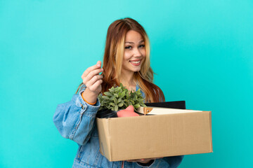 Teenager blonde girl making a move while picking up a box full of things making money gesture