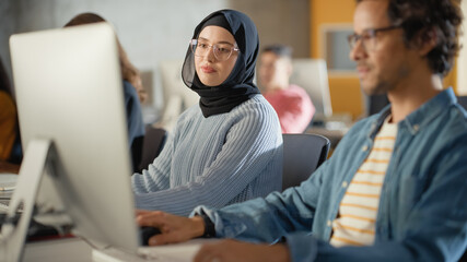 Curious Female Muslim Student Wearing a Hijab, Studying in Modern University with Diverse Multiethnic Classmates. College Scholars Work in College Room, Learning IT, Programming or Computer Science.