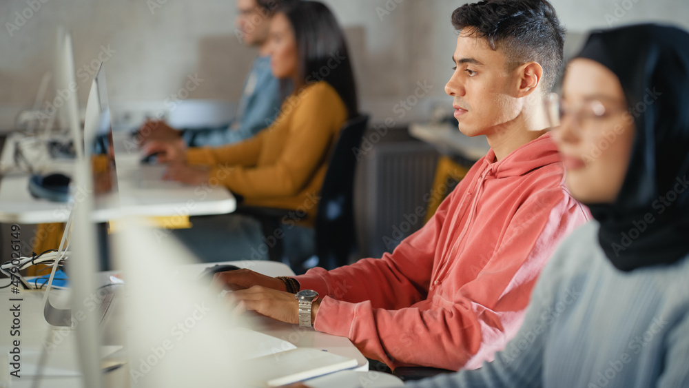 Wall mural Handsome Smart Male Student, Studying in University with Diverse Multiethnic Classmates. He Works on Desktop Computer in College. Applying His Knowledge to Acquire Academic Skills in Class.