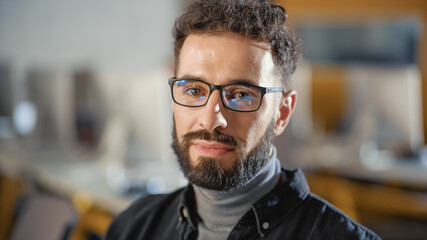 Obraz premium Portrait of a Happy Handsome Smart Male, Seriously Looking on Camera Indoors. Confident Successful Man Wears and Turtleneck and Glasses, Has a Bushy Beard and Short Curly Hair.