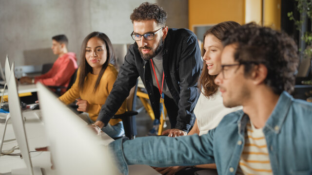 Lecturer Helps Scholar With Project, Advising On Their Work. Teacher Giving Lesson To Diverse Multiethnic Group Of Female And Male Students In College Room, Teaching New Academic Skills On A Computer.