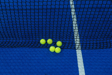 Multiple balls in the net of a blue paddle tennis court.