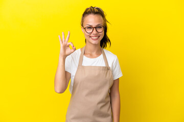 Restaurant waiter Russian girl isolated on yellow background showing ok sign with fingers