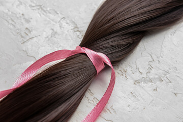 Brunette hair strand for donation with pink ribbon on grunge background, closeup