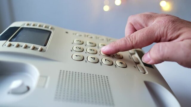 closeup female hand presses the buttons of the stationary white office Wired phone, dials the subscriber's number for communication, the concept of hotline help, call center, selective focus