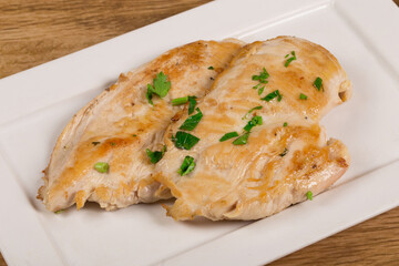 Grilled chicken breast on white dish on wooden background.