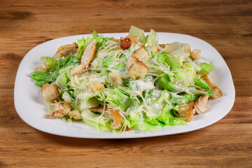 fresh caesar salad with chicken pieces served on white dish on wooden background
