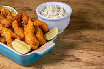  View of crispy fish , fish fingers or strips served with tartar sauce and lemon slices. Kid meal, appertiser or snack food made using a whitefish