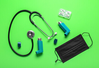 Asthma inhalers, stethoscope, pills and mask on green background