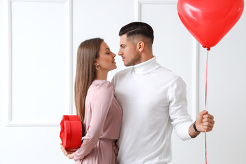 Fototapeta Happy young couple with gift and balloon on light background. Valentine's Day celebration obraz