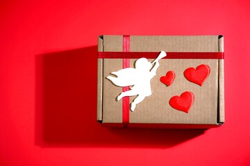 Present for Saint Valentines Day, craft cardboard love box, gift for holiday with hearts and angel toy on red background. 14 February. Happy Valentines day . Top view. Copy space.