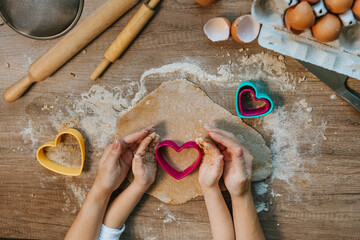 Fototapeta Top view of little girl with parent cutting heart shape cookies from rye dough obraz