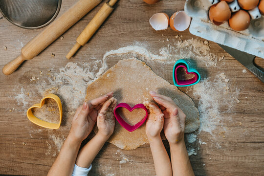 Top view of little girl with parent cutting heart shape cookies from rye dough