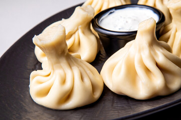 khinkali with white sauce on a dark plate on a light background