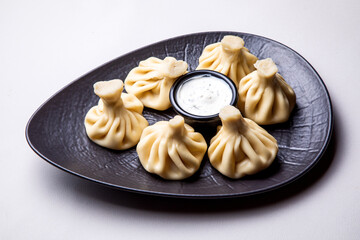 khinkali with white sauce on a dark plate on a light background