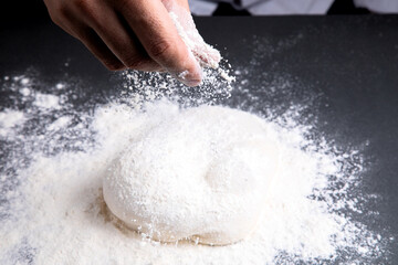 man sprinkles flour on the dough and table. dark background
