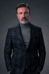 Fototapeta premium Portrait of a stylish elegant senior businessman with a beard and casual business clothes in photo studio isolated on dark background gesturing with hands