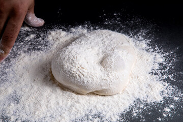 man sprinkles flour on the dough and table. dark background