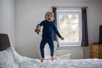 Fototapeta na wymiar Happy toddler child, blond boy with blue pajama, jumping on the bed