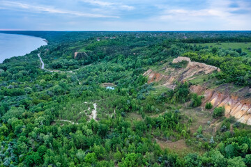 Colorful clay hills overgrown with green trees. Natural abstract landscape, aerial view from drone