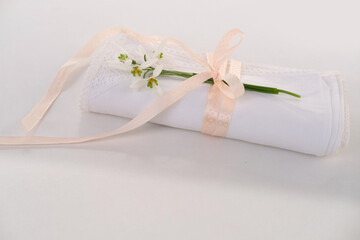 white linen napkin, finished with handmade lace, rolled in several layers, a delicate snowdrop flower is on a light table, the concept of luxury setting, a spring gift