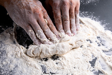 the chef kneads the dough on a dark background, the table is strewn with flour